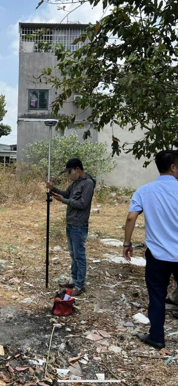 Nhân sự khảo sát cầm sào gắn thiết bị định vị vệ tinh tại khu đất cạnh nhà ở.
